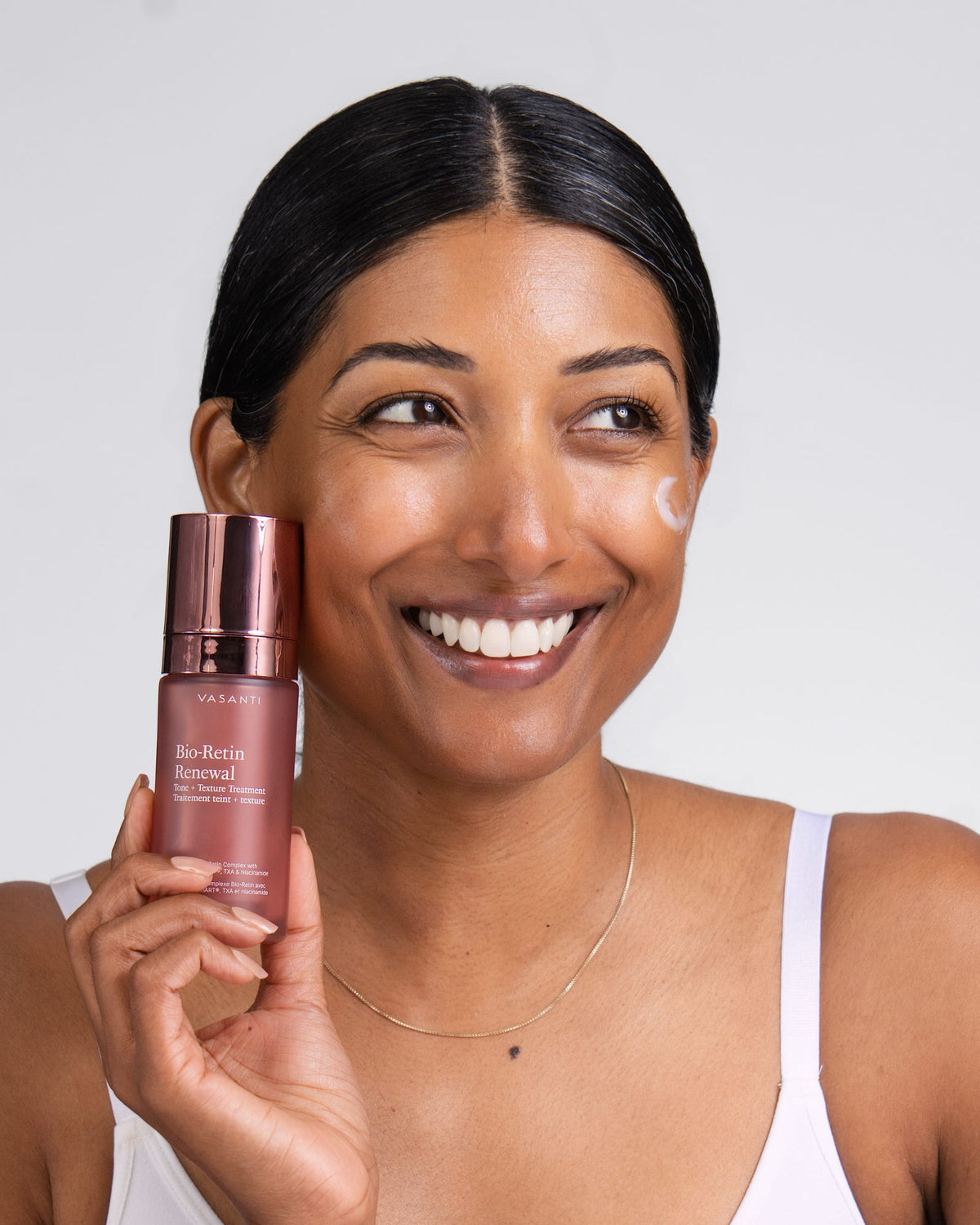 Smiling woman holding Bio-Retin Renewal, a dot of the cream on her cheek